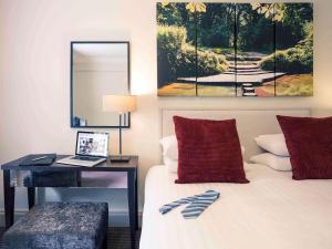1 dormitorio con cama, escritorio y espejo en Mercure Box Hill Burford Bridge Hotel en Dorking