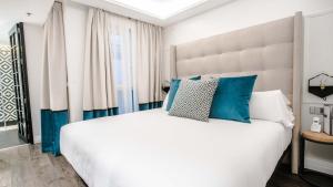 een slaapkamer met een groot wit bed met blauwe kussens bij Hotel Regina in Madrid