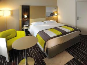 グランビルにあるメルキュール グランビル ル グラン ラージのベッドと緑の椅子が備わるホテルルームです。