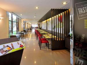 a restaurant with a row of tables and red chairs at Ibis Bangkok Riverside in Bangkok