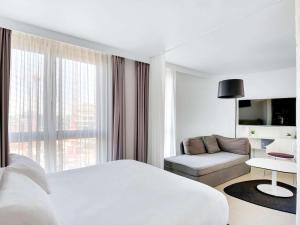 Cette chambre blanche comprend un lit et un canapé. dans l'établissement Novotel Suites Paris Issy Les Moulineaux, à Issy-les-Moulineaux