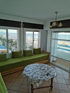 ein Wohnzimmer mit einem grünen Sofa und Fenstern in der Unterkunft Appartement CORNICHE vue sur MER in Martil