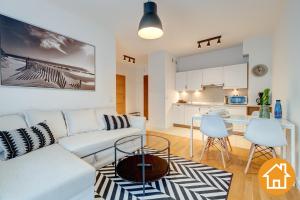 a living room with a white couch and a kitchen at Apartamenty Aquamarina - visitopl in Międzyzdroje