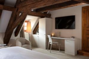 a room with a bed, chair, lamp and a tv at Relais & Châteaux La Maison Des Têtes in Colmar