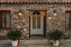 a stone building with a white door and two potted plants at Charco Hotel in Colonia del Sacramento