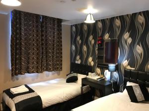 a room with two beds and a desk and curtains at Pacific Inn London Heathrow in Southall