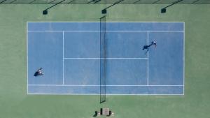 two men playing tennis on a blue tennis court at Anantara Desert Islands Resort & Spa in Da‘sah