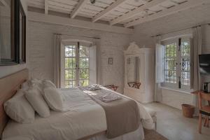 a white bedroom with a large bed and two windows at Charco Hotel in Colonia del Sacramento