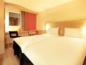 a hotel room with a large white bed and a desk at Ibis Lleida in Lleida