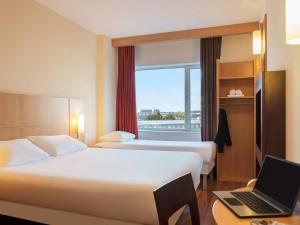 a hotel room with two beds and a laptop on a desk at ibis Leiden Centre in Leiden