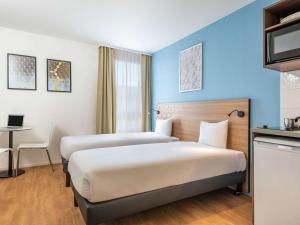 a hotel room with two beds and a desk at Aparthotel Adagio Access Paris Quai d'Ivry in Ivry-sur-Seine