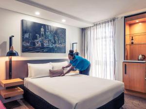 una mujer está haciendo una cama grande en una habitación de hotel en Mercure Brisbane King George Square, en Brisbane
