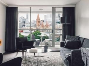 a living room with a couch and chairs and a large window at Quay West Suites Melbourne in Melbourne