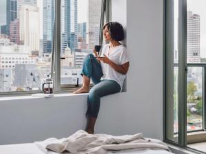 a woman sitting on a window sill holding a cell phone at Quay West Suites Melbourne in Melbourne