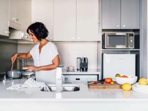 a woman standing in a kitchen preparing food at Quay West Suites Melbourne in Melbourne