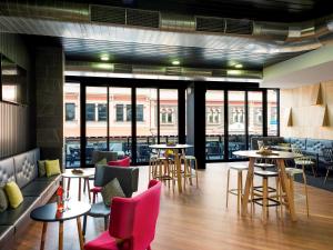 un restaurante con mesas, sillas y ventanas en ibis Adelaide en Adelaida