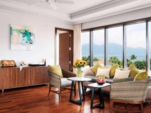 een woonkamer met een bank, stoelen en ramen bij Pullman Danang Beach Resort in Da Nang