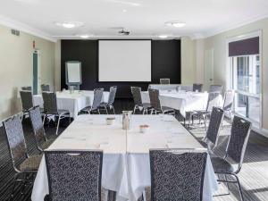 a conference room with tables and chairs and a projection screen at Mercure Wagga Wagga in Wagga Wagga