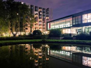 ein Gebäude mit einer Spiegelung im Wasser in der Nacht in der Unterkunft Mercure Hotel Dortmund Messe in Dortmund