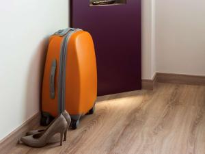 einen orangenen Koffer und ein Paar Schuhe vor einer Tür in der Unterkunft Hotel Ibis Styles Lleida Torrefarrera in Lleida