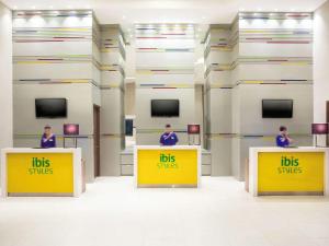 three people standing behind yellow counters with the words bus slips at Ibis Styles Jakarta Mangga Dua Square in Jakarta