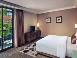 a bedroom with a bed and a television and a balcony at Mercure Bali Legian in Legian