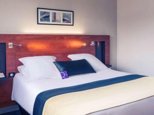 a large white bed with a blue pillow on it at Mercure Maurepas Saint Quentin in Maurepas