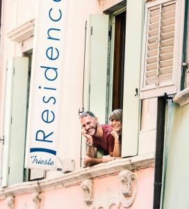 a man and a woman looking out of a window at Residence Trieste in Riva del Garda