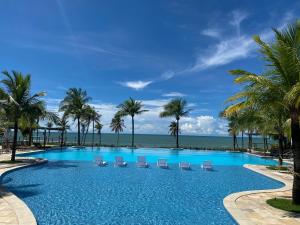 a swimming pool with palm trees and chairs and the ocean at Condomínio Wai Wai Pé na Areia - Praia de Cumbuco in Cumbuco