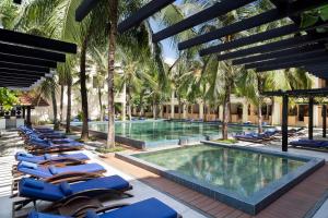 
a pool with chairs, tables, and umbrellas at Anantara Hoi An Resort in Hoi An

