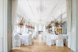 un salón de banquetes con mesas y sillas blancas y una lámpara de araña en Hotel Schloss Teutschenthal, en Teutschenthal