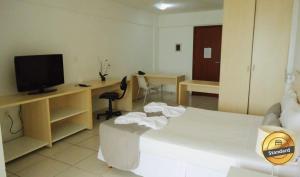 Habitación con cama, TV y escritorio. en Terrazzo Ponta Negra Flat JD, en Natal