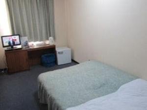 a hotel room with a bed and a desk and a television at Asahikan in Kofu