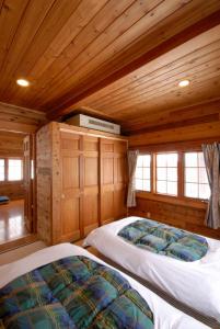 two beds in a room with wooden walls and windows at Hakuba Brownie Cottages in Hakuba