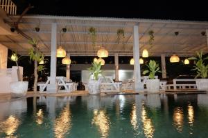 uma piscina com cadeiras brancas, mesas e luzes em Pom Pom's Bali Apartments em Kerobokan