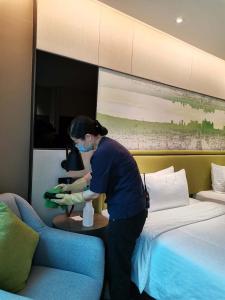 a woman is standing next to a bed at Hampton by Hilton Guangzhou Tianhe Sports Center in Guangzhou