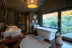 a bathroom with a tub and a sink and a window at HillsNek Safari Camp – Amakhala Game Reserve in Amakhala Game Reserve
