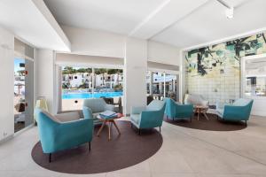 a waiting room with blue chairs and tables at TRH Tirant Playa in Fornells