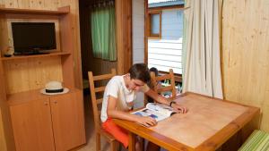 a man sitting at a table cutting a piece of paper at Camping Bon Repós in Santa Susanna