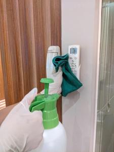 une main tenant une brosse verte de nettoyage dans une chambre dans l'établissement Happy Inn, à Jakarta