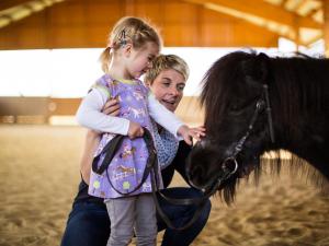een vrouw die een klein meisje vasthoudt die een paard aait bij Landhaus Schulte-Göbel in Schmallenberg