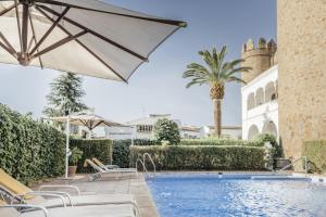 a pool with chairs and an umbrella next to a building at Parador de Zafra in Zafra