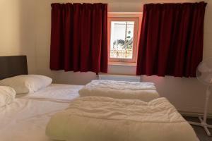 two beds in a room with red curtains and a window at Hermes Appartementen in Berg en Terblijt