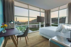 a hotel room with a bed and a desk and windows at NH Collection Santiago Casacostanera in Santiago