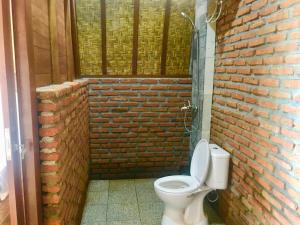 a bathroom with a toilet and a brick wall at Arjuna Uluwatu Guest House in Uluwatu