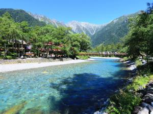 a bridge over a river with mountains in the background at Guesthouse Tomoshibi in Matsumoto