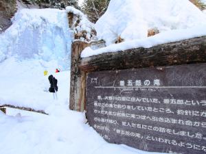 a sign covered in snow next to a waterfall at Guesthouse Tomoshibi in Matsumoto