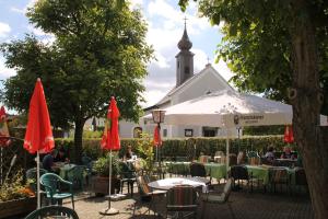 a group of tables with red umbrellas in front of a church at Gasthof Pension Renate Krupik in Steinbach
