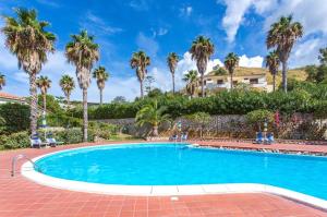 a swimming pool with palm trees and a house in the background at Residence Antigua in Bonifati