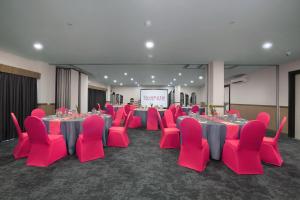 una sala de conferencias con mesas y sillas rosas y una pantalla en favehotel Malang, en Malang